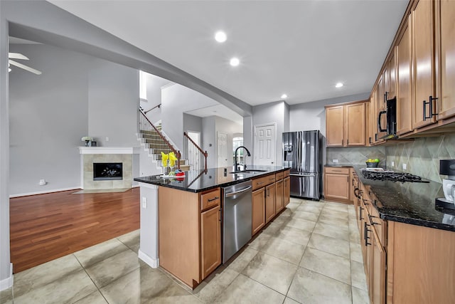 kitchen featuring a sink, open floor plan, dark stone counters, black appliances, and an island with sink