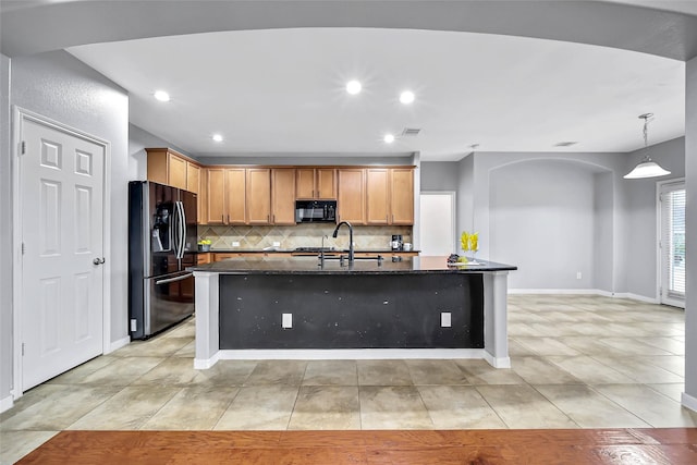 kitchen featuring stainless steel fridge with ice dispenser, an island with sink, decorative light fixtures, black microwave, and backsplash