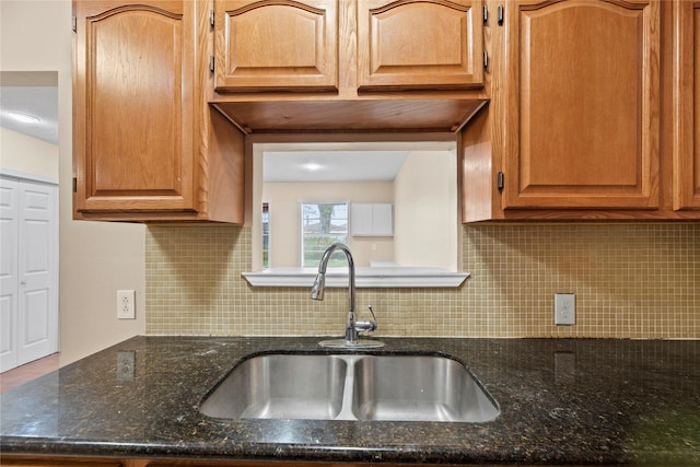 kitchen featuring backsplash, dark stone countertops, and sink