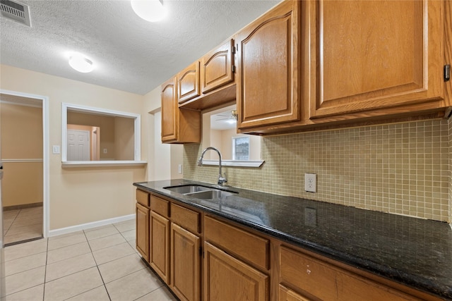 kitchen with dark stone counters, sink, decorative backsplash, light tile patterned floors, and a textured ceiling