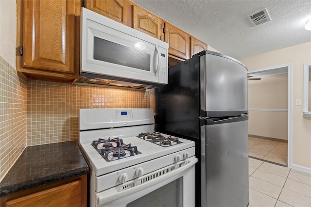 kitchen featuring backsplash, white appliances, a textured ceiling, light tile patterned floors, and dark stone countertops