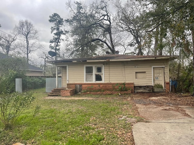 rear view of house featuring brick siding, a lawn, and fence