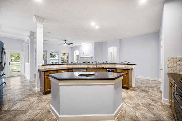 kitchen with ornate columns, dark stone counters, ceiling fan, sink, and a center island with sink