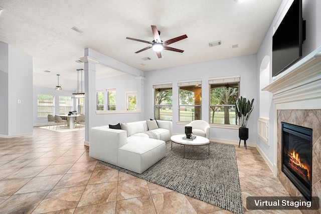 living room with a tiled fireplace, ceiling fan, light tile patterned flooring, and a textured ceiling