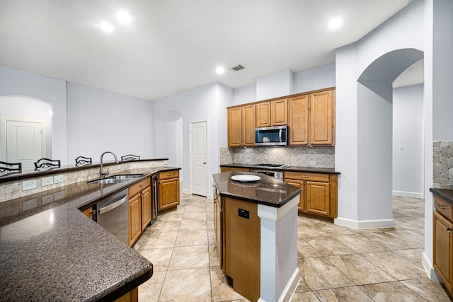 kitchen featuring a center island with sink, sink, dark stone countertops, tasteful backsplash, and stainless steel appliances