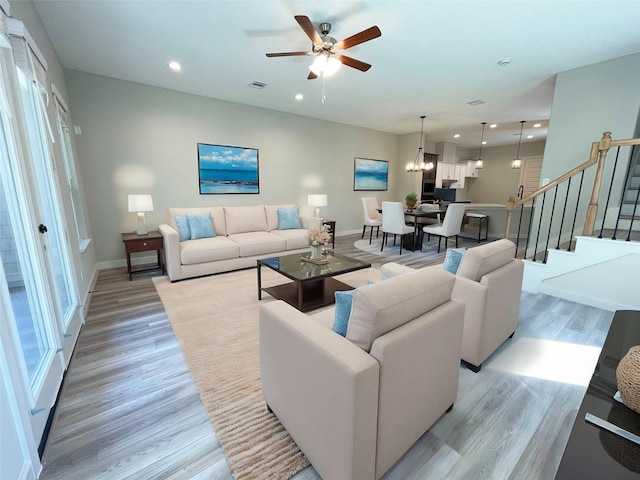 living room with ceiling fan with notable chandelier, light hardwood / wood-style flooring, and plenty of natural light