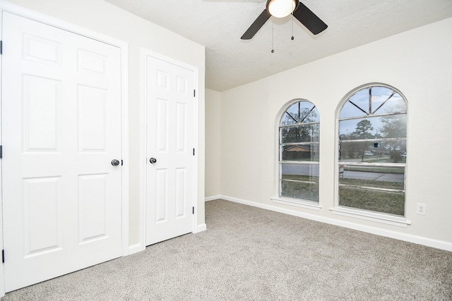 unfurnished bedroom featuring multiple closets, ceiling fan, light carpet, and a textured ceiling