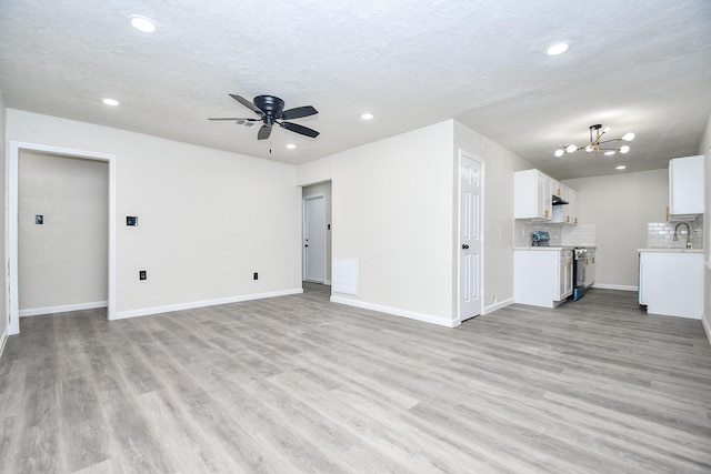 unfurnished living room featuring ceiling fan with notable chandelier, light wood-type flooring, a textured ceiling, and sink