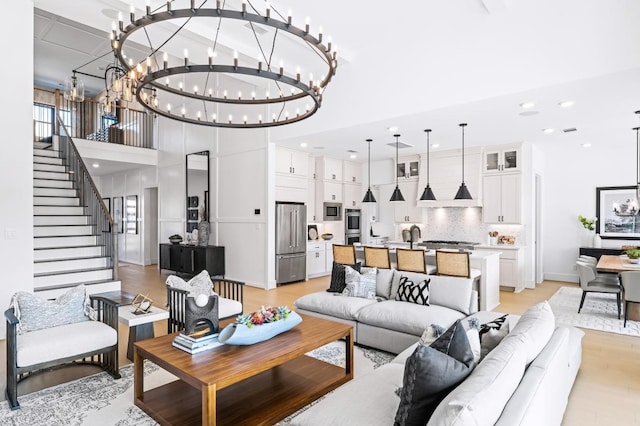 living room featuring a notable chandelier, light wood-type flooring, sink, and a towering ceiling