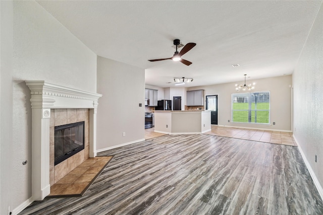 unfurnished living room with ceiling fan with notable chandelier, light wood-type flooring, and a tile fireplace