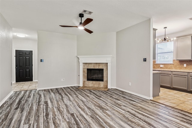 unfurnished living room with ceiling fan with notable chandelier, light hardwood / wood-style floors, and a tile fireplace