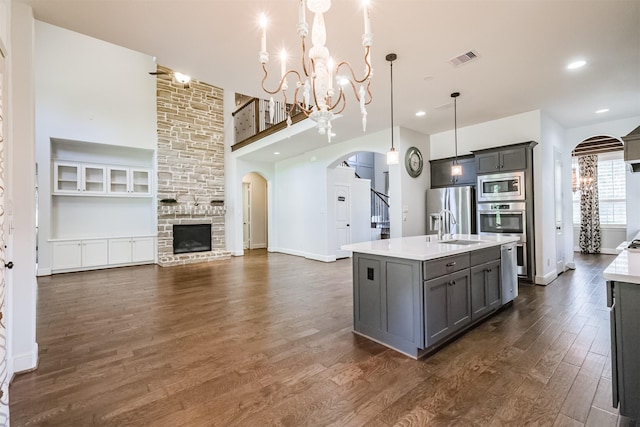 kitchen featuring appliances with stainless steel finishes, gray cabinetry, pendant lighting, a center island with sink, and a chandelier