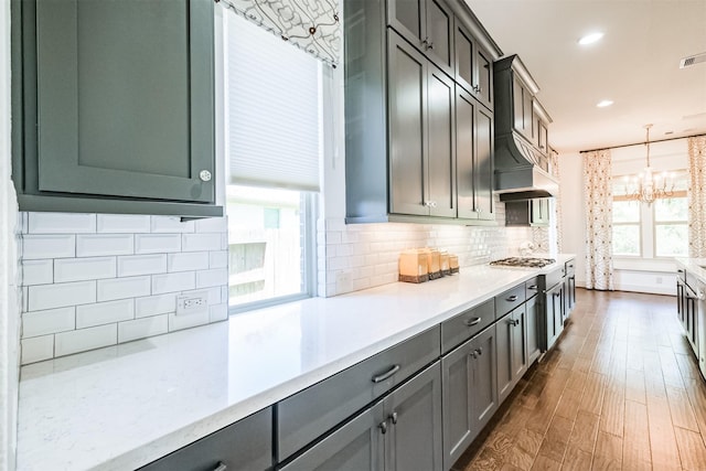 kitchen featuring stainless steel gas cooktop, tasteful backsplash, an inviting chandelier, dark hardwood / wood-style floors, and pendant lighting