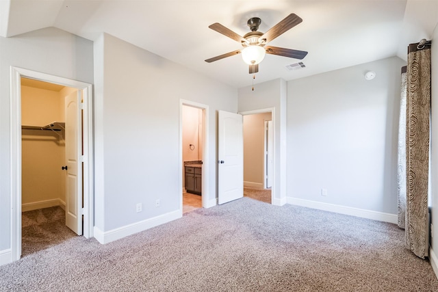 unfurnished bedroom featuring ensuite bath, ceiling fan, light colored carpet, a walk in closet, and a closet