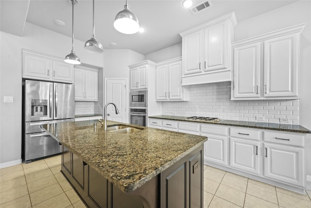 kitchen featuring white cabinetry, an island with sink, stainless steel appliances, dark stone countertops, and sink