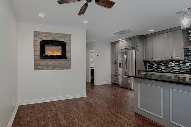 kitchen with dark wood-type flooring, stainless steel fridge, gray cabinets, backsplash, and a fireplace