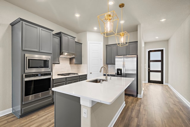 kitchen with sink, a notable chandelier, pendant lighting, a kitchen island with sink, and appliances with stainless steel finishes