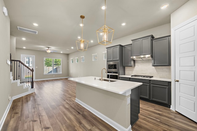 kitchen with appliances with stainless steel finishes, tasteful backsplash, gray cabinetry, ceiling fan with notable chandelier, and hanging light fixtures