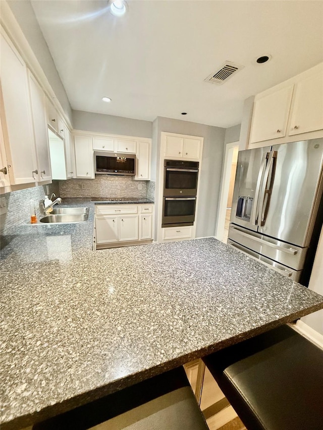 kitchen with appliances with stainless steel finishes, white cabinetry, a kitchen breakfast bar, and sink