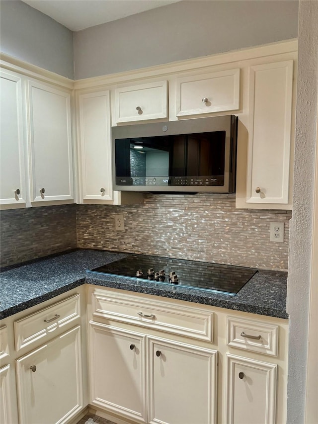 kitchen featuring dark stone counters, cream cabinets, black stovetop, and decorative backsplash