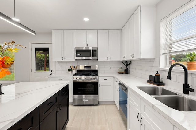 kitchen with sink, appliances with stainless steel finishes, tasteful backsplash, light stone counters, and white cabinetry