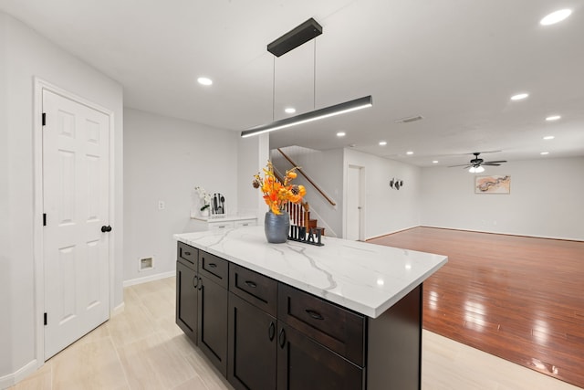 kitchen with ceiling fan, light stone counters, pendant lighting, a kitchen island, and light wood-type flooring