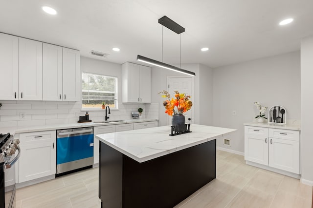 kitchen featuring sink, stainless steel appliances, a kitchen island, decorative light fixtures, and white cabinets