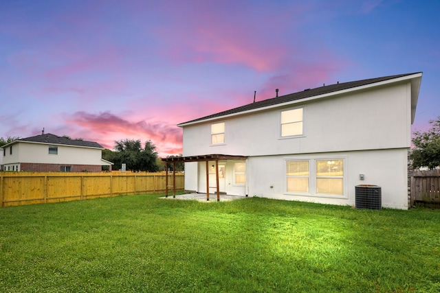 back house at dusk with a yard, central AC unit, and a patio area