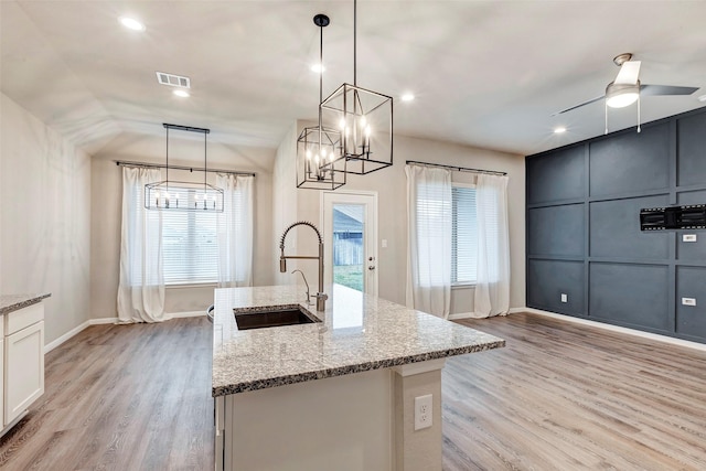 kitchen with ceiling fan with notable chandelier, sink, light stone countertops, decorative light fixtures, and light hardwood / wood-style floors