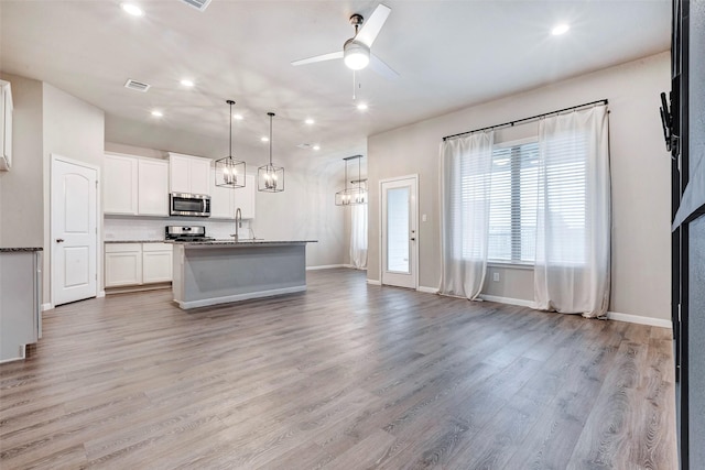 kitchen featuring white cabinetry, stainless steel appliances, light hardwood / wood-style floors, decorative light fixtures, and a center island with sink