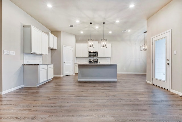 kitchen featuring white cabinetry, a center island with sink, pendant lighting, and light hardwood / wood-style floors