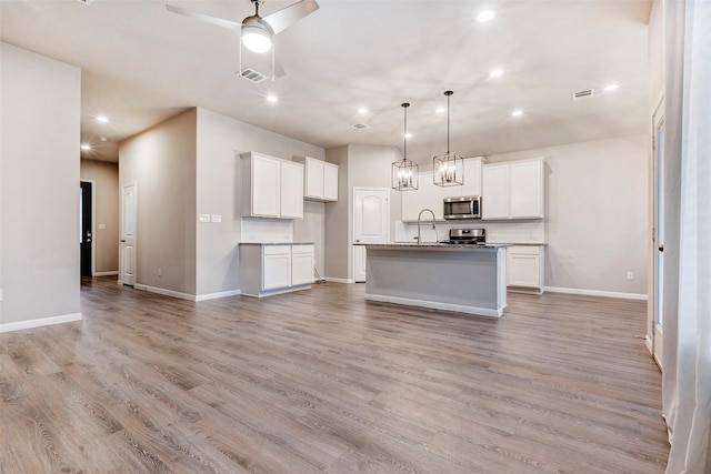 kitchen with decorative backsplash, light wood-type flooring, stainless steel appliances, white cabinets, and an island with sink