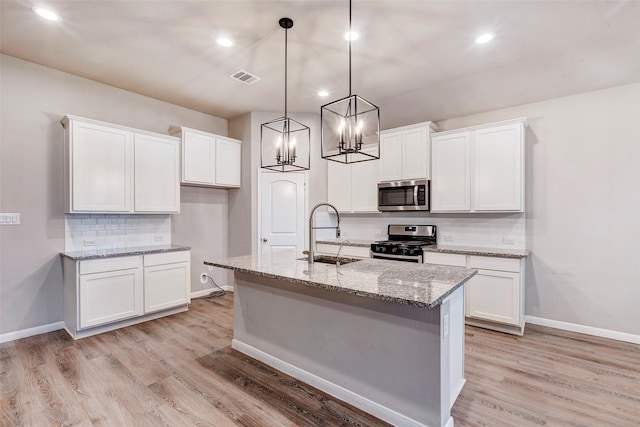 kitchen featuring stainless steel appliances, a kitchen island with sink, sink, white cabinets, and hanging light fixtures