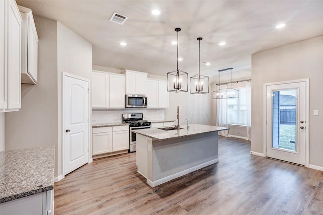 kitchen with light stone counters, stainless steel appliances, sink, decorative light fixtures, and white cabinets