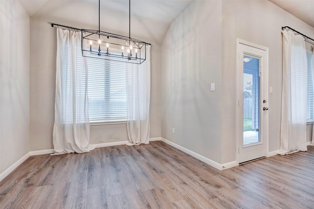 unfurnished dining area featuring a healthy amount of sunlight, light hardwood / wood-style floors, vaulted ceiling, and a notable chandelier