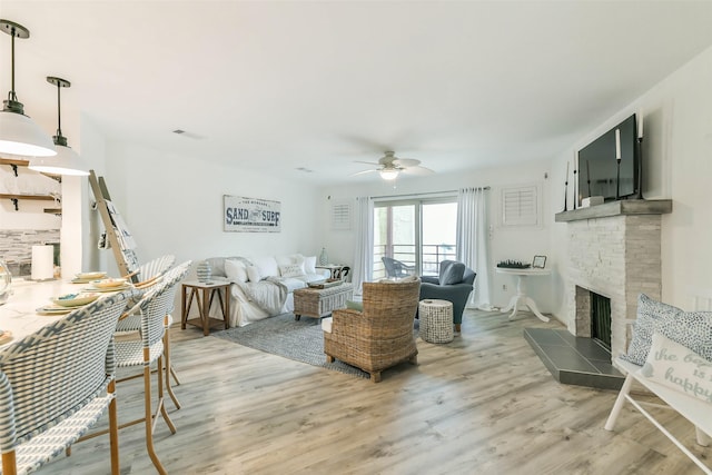 living room featuring ceiling fan, light hardwood / wood-style flooring, and a stone fireplace