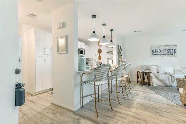 kitchen featuring white cabinets, a kitchen breakfast bar, light wood-type flooring, and hanging light fixtures