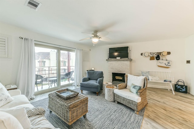 living room with hardwood / wood-style floors, ceiling fan, and a stone fireplace