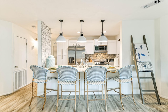 kitchen featuring stainless steel appliances, a breakfast bar, hanging light fixtures, and white cabinetry