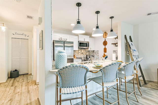 kitchen featuring stainless steel appliances, white cabinets, light wood-type flooring, backsplash, and pendant lighting