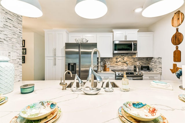 kitchen with appliances with stainless steel finishes, white cabinetry, light stone counters, and backsplash