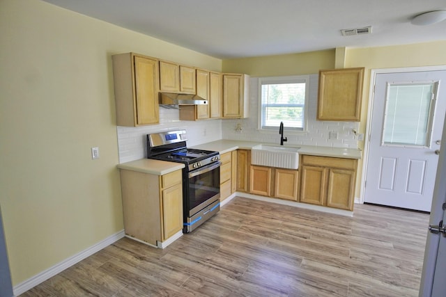 kitchen featuring light brown cabinetry, backsplash, sink, stainless steel gas stove, and light hardwood / wood-style floors