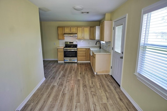 kitchen with light brown cabinets, backsplash, sink, stainless steel stove, and light wood-type flooring