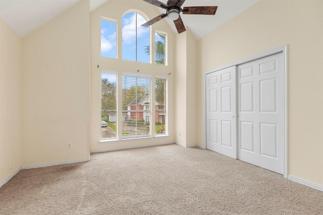 unfurnished bedroom featuring ceiling fan, light colored carpet, high vaulted ceiling, and a closet