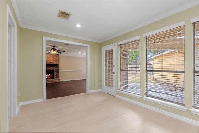 unfurnished room featuring a brick fireplace, ceiling fan, a textured ceiling, and ornamental molding