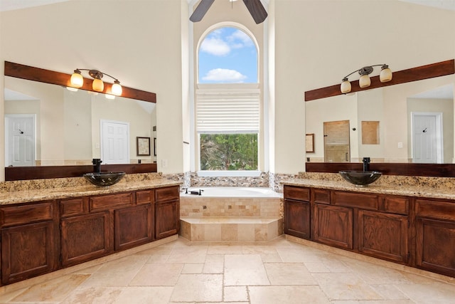 bathroom featuring ceiling fan, vanity, tiled tub, and high vaulted ceiling