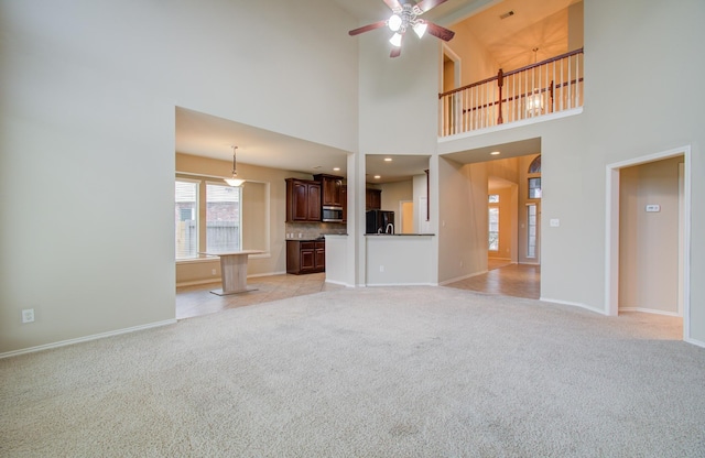 unfurnished living room featuring light carpet, a towering ceiling, and ceiling fan