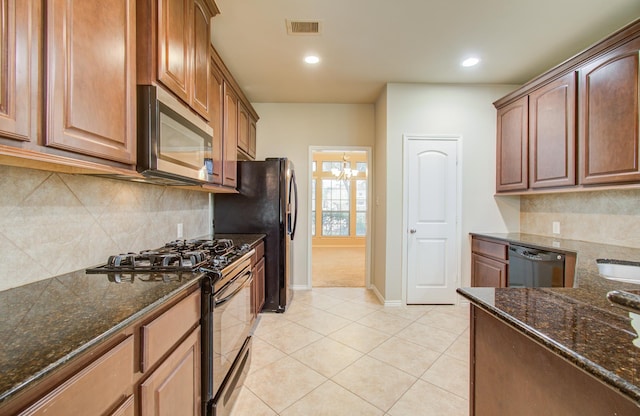 kitchen with decorative backsplash, appliances with stainless steel finishes, an inviting chandelier, dark stone countertops, and light tile patterned flooring