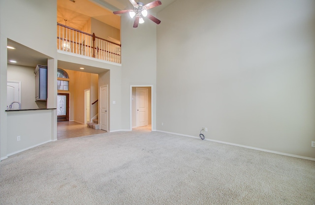 unfurnished living room featuring carpet flooring, ceiling fan, and a high ceiling