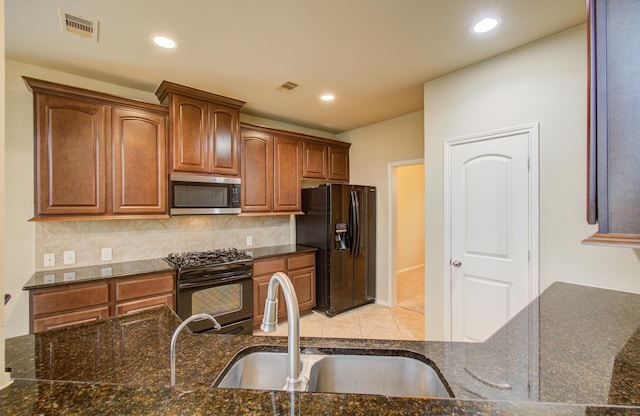 kitchen featuring sink, backsplash, dark stone countertops, and black appliances